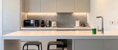 A modern kitchen with a white countertop, built-in appliances, and a bar area with stools.