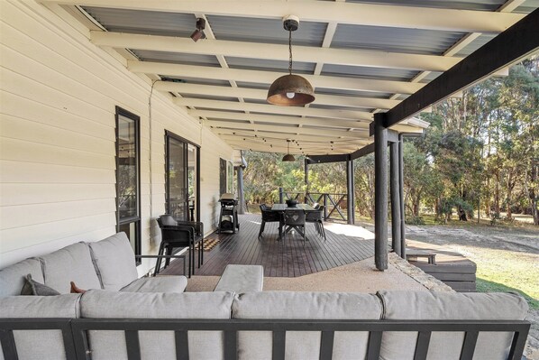 A covered outdoor seating area with a table and chairs, a sofa, and a pergola structure.