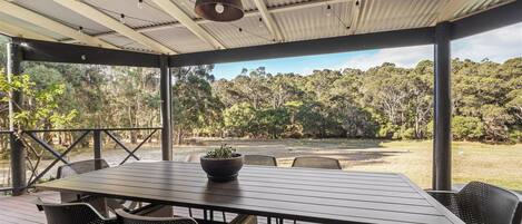 A covered outdoor area with a table and chairs, a hanging light fixture, and a view of a forested landscape.