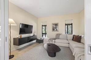 A modern living room with a flat-screen TV, a sofa, a coffee table, and a lamp.