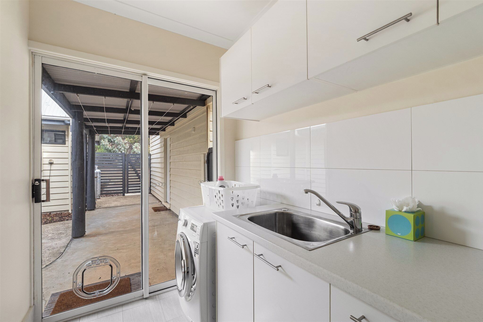 A compact kitchen with a washing machine, a sink, and a small trash bin.