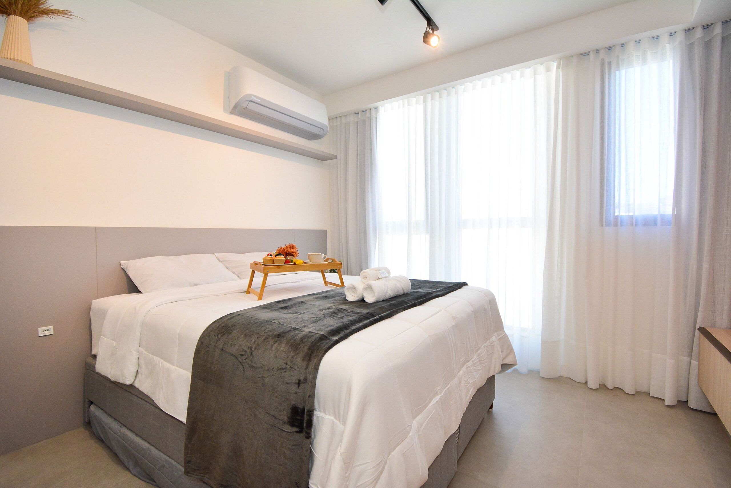 Ein modernes Hotelzimmer mit Bett, Nachttisch, Tablett mit Handtüchern und einem fenster mit Vorhängen.