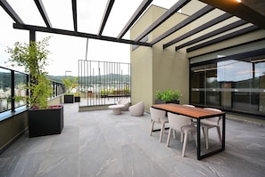 Una terraza moderna al aire libre con zona de comedor, asientos y plantas en macetas.