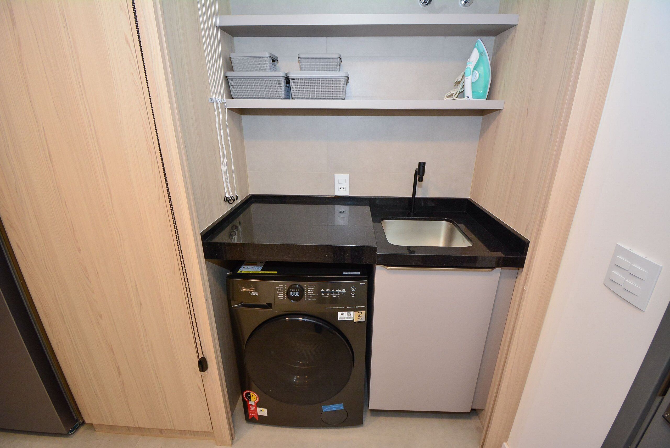 Una cocina compacta con lavadora, lavamanos y estanterías.