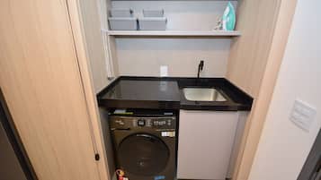 A compact kitchen with a washing machine, a sink, and storage shelves.