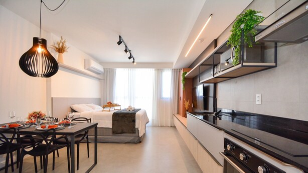 A modern kitchen with a black stove, a dining area with a table and chairs, and a bed with a white headboard. - Studio em frente a UFSC e HU - 709A (Florianópolis)