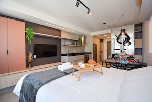 Una habitación de hotel moderna con una cama, una mesita de noche y un comedor con una mesa dispuesta para dos.