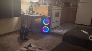 Eine Küche mit Kühlschrank, Herd und Schränken. Ein Tisch steht dort mit einer Lampe und einem Computer.