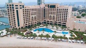 Un hotel grande con varias plantas, una piscina central y una zona de playa con tumbonas.