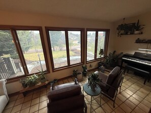 Ein Wohnzimmer mit einem Klavier, großen Fenstern und Zimmerpflanzen.