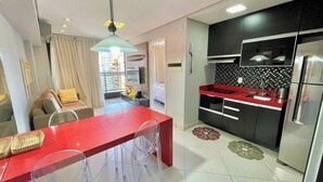 Eine moderne Küche mit roter Arbeitsplatte, Edelstahlgeräten und einem Essbereich mit rotem Tisch und klaren Stühlen.