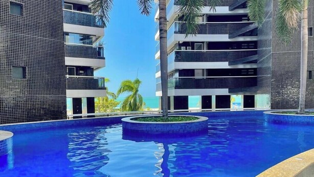 Ein modernes Hotel mit einem zentral gelegenen Schwimmbad, mehreren Balkonen und Meerblick.