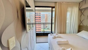 Ein Hotelzimmer mit Bett, Blick auf Gebäude, einem Balkon und einem fenster mit Vorhängen.
