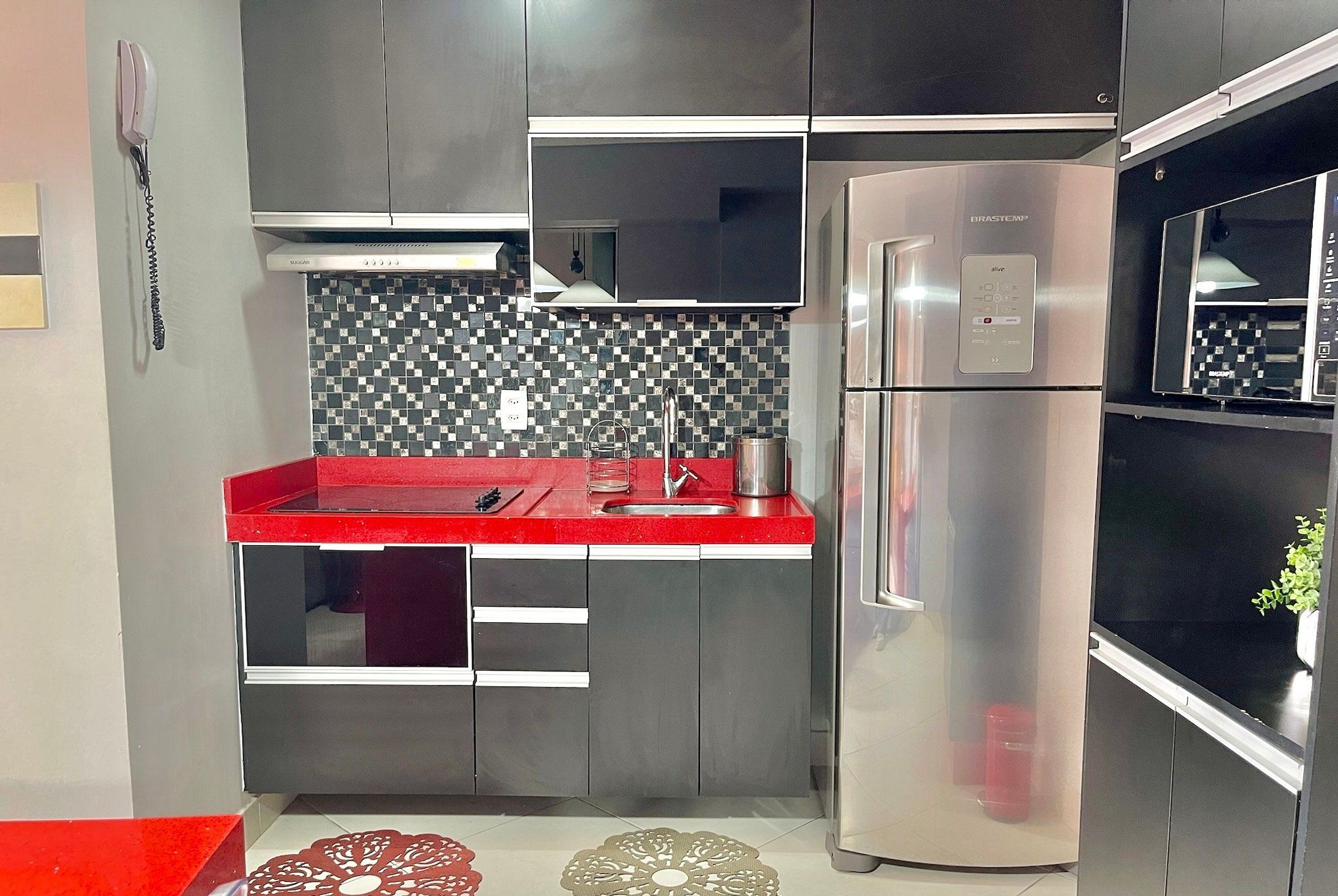 A modern kitchen with stainless steel appliances, a red countertop, and a patterned backsplash.