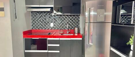 A modern kitchen with stainless steel appliances, a red countertop, and a patterned backsplash.