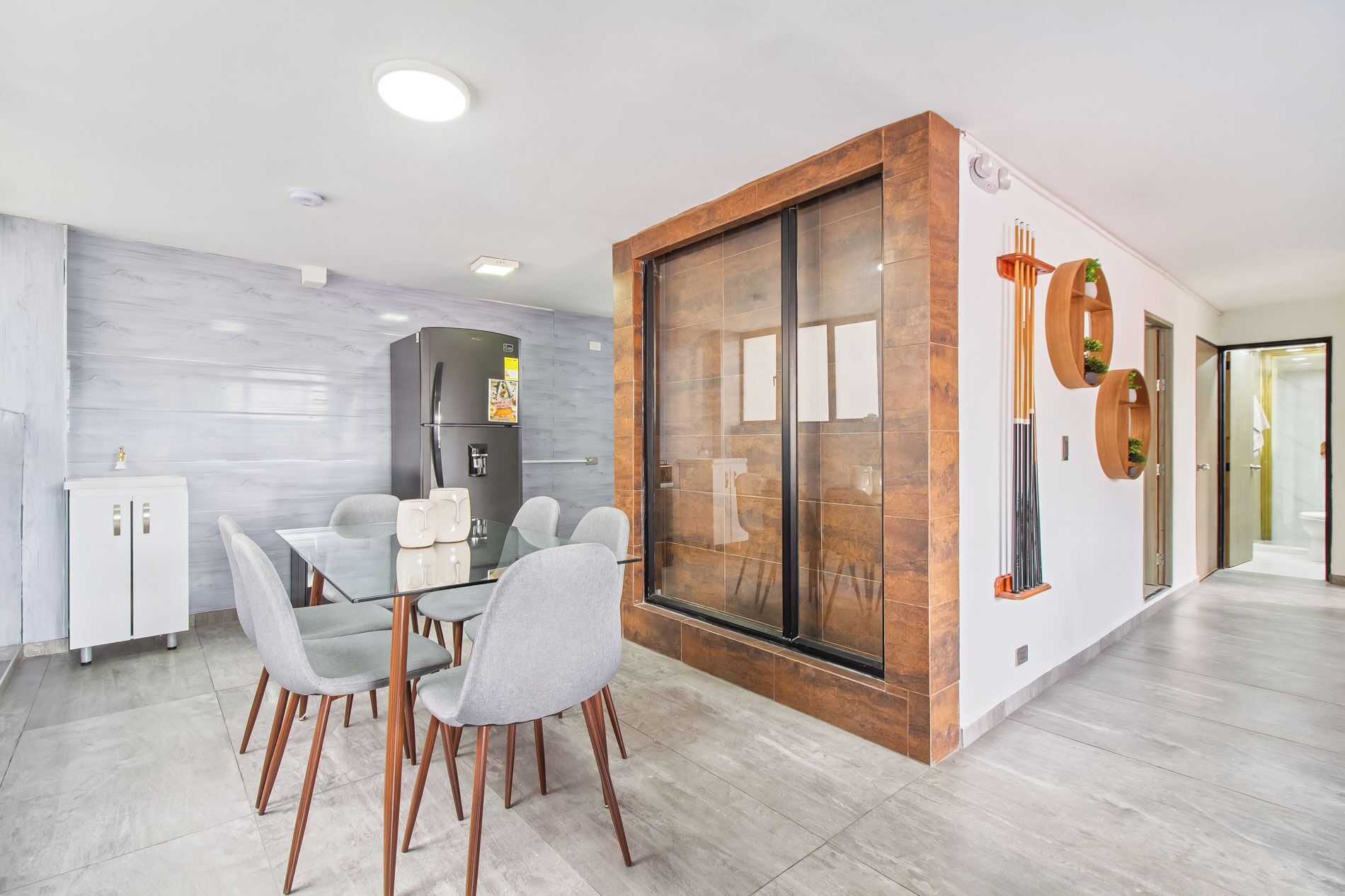 Una cocina moderna con una mesa de comedor de vidrio, sillas grises y un refrigerador empotrado.