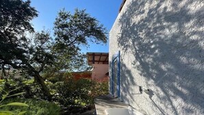 A narrow pathway leading to a building with a white exterior and blue shutters. - Completely renovated house with garden surrounded by pine forest, facing the sea (Matta E Peru)
