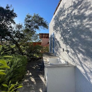 A narrow pathway leading to a building with a white exterior and blue shutters. - Completely renovated house with garden surrounded by pine forest, facing the sea (Matta E Peru)