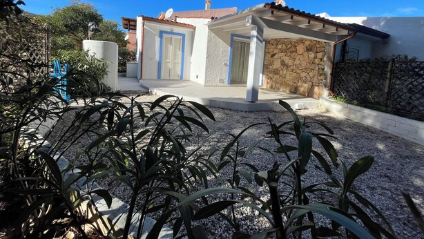A house with a stone wall, a blue door, and a covered porch. - Completely renovated house with garden surrounded by pine forest, facing the sea (Matta E Peru)