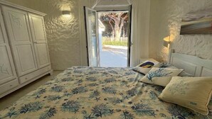 A bedroom with a bed, a wardrobe, and a view through an open door. - Completely renovated house with garden surrounded by pine forest, facing the sea (Matta E Peru)