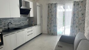 A modern kitchen with white cabinets, a black faucet, and a grey countertop. There is a grey sofa with a pair of glasses on it. - Completely renovated house with garden surrounded by pine forest, facing the sea (Matta E Peru)