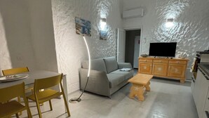 A living room with a sofa, a dining table with chairs, a TV on a wooden cabinet, and a patterned rug. - Completely renovated house with garden surrounded by pine forest, facing the sea (Matta E Peru)