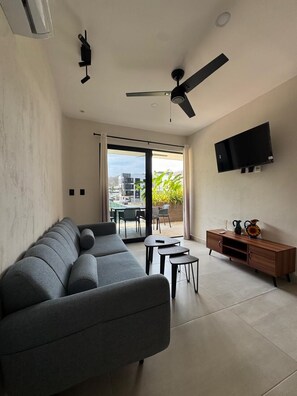 A modern living room with a sofa, a small table, a TV, and a ceiling fan. - The heart of Santa Cruz steps from the beach! (Crucecita)