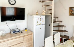 Ein kompakter Wohnbereich mit Flachbildfernseher, einem weißen Kühlschrank mit Magneten, einem Holzschrank und einem kleinen Tisch mit Stuhl.