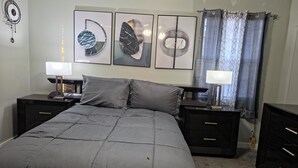 A bedroom with a bed, two bedside tables, a wall clock, and three framed artworks.