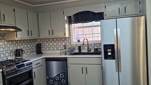 A kitchen with white cabinets, a stainless steel refrigerator, a stove, and a dishwasher.