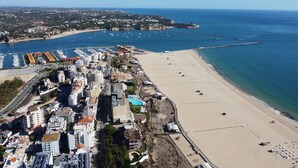 An aerial view of a coastal city with a marina, sandy beach, and residential buildings. - Apartment Praia Rocha | Near Beach | Safira V (Portimão)