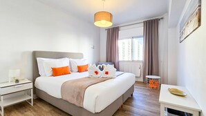 A modern hotel room with a large bed, bedside tables, a small desk, and a window with curtains. - Apartment Praia Rocha | Near Beach | Safira V (Portimão)