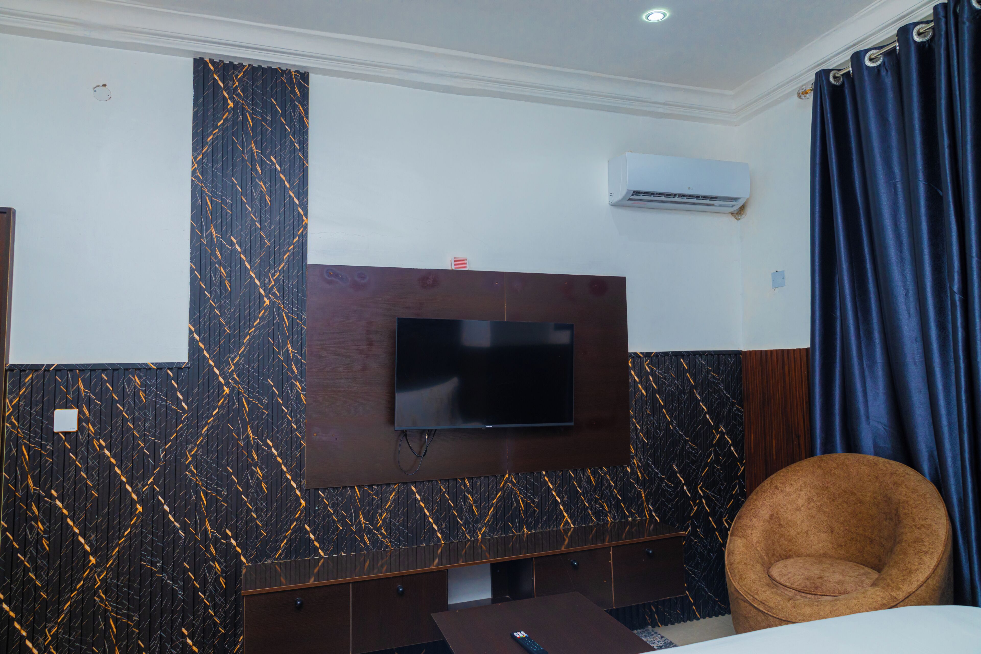 A hotel room with a flat-screen TV mounted on the wall, a brown armchair, a small table, and a bed.