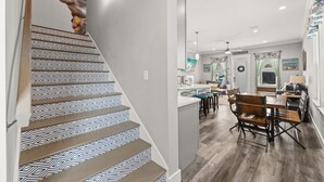 Eine Treppe mit geometrischen Fliesenmustern und einem hölzernen Geländer, die zu einem Küchenbereich mit Bar und Sitzgelegenheiten führt.