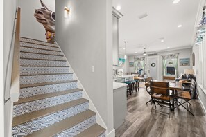 A staircase with geometric patterned tiles and a wooden handrail, leading to a kitchen area with a bar and seating. - Rooftop Deck, Game Room, Fire Pit, Sleeps 16 (Panama City Beach)