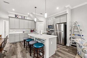 A modern kitchen with white cabinets, a central island with stools, stainless steel appliances, and a ladder against the wall. - Rooftop Deck, Game Room, Fire Pit, Sleeps 16 (Panama City Beach)
