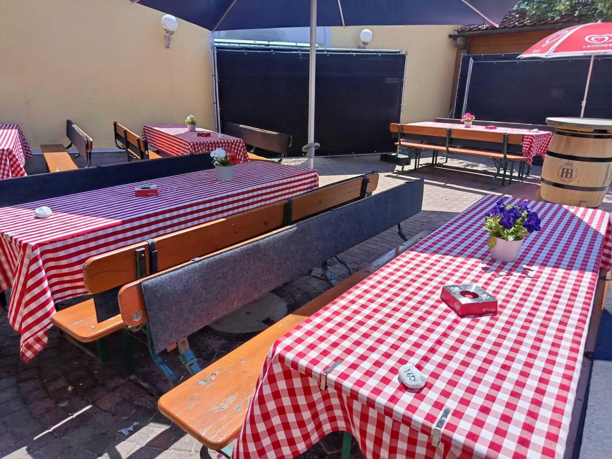 Espace extérieur aménagé avec des tables recouvertes de nappes à carreaux, des bancs en bois et des parasols.