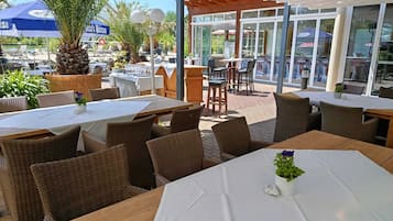 Un espace de restauration en plein air, avec des meubles en osier, des nappes blanches et une vue sur la mer.