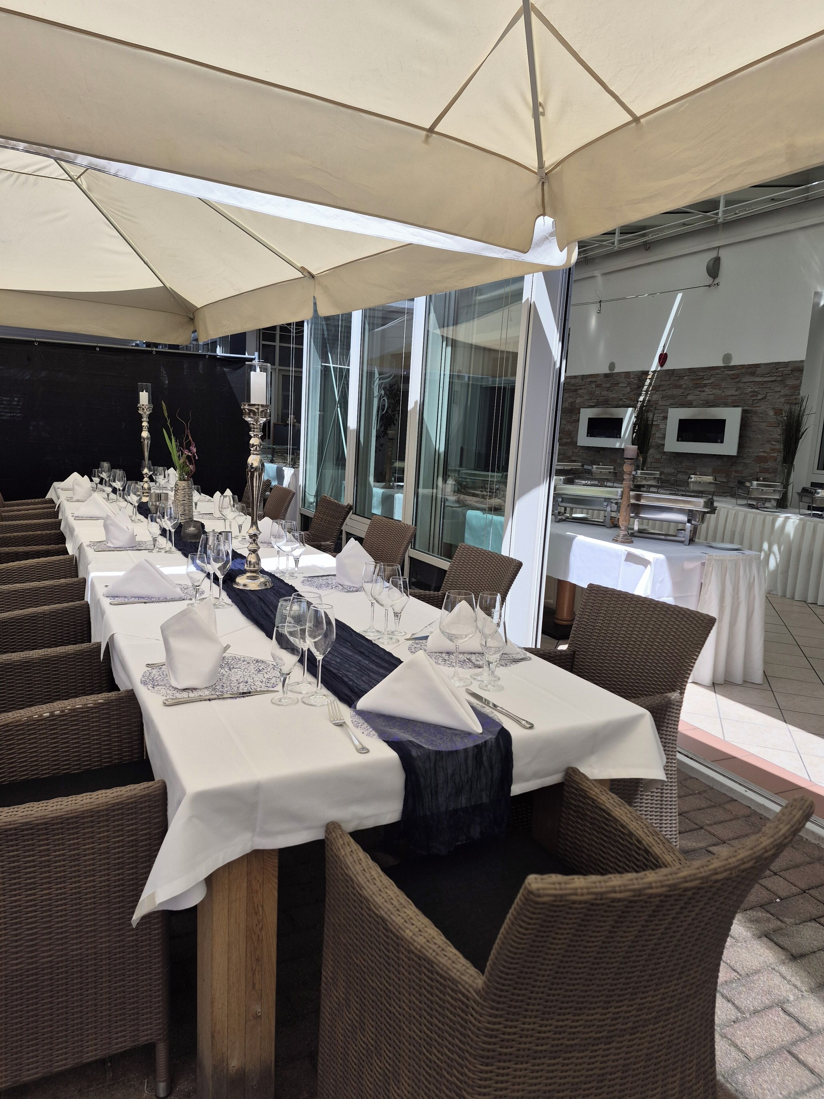 A restaurant with outdoor seating, covered by a large canopy, and tables set with white tablecloths and silverware.