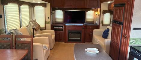 Interior compacto de una caravana con kitchenette, zona de estar y televisor.