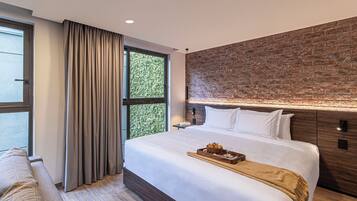 Una habitación de hotel moderna con una cama grande, una pared de ladrillo decorativa, una ventana con cortinas y una mesita de noche de madera.