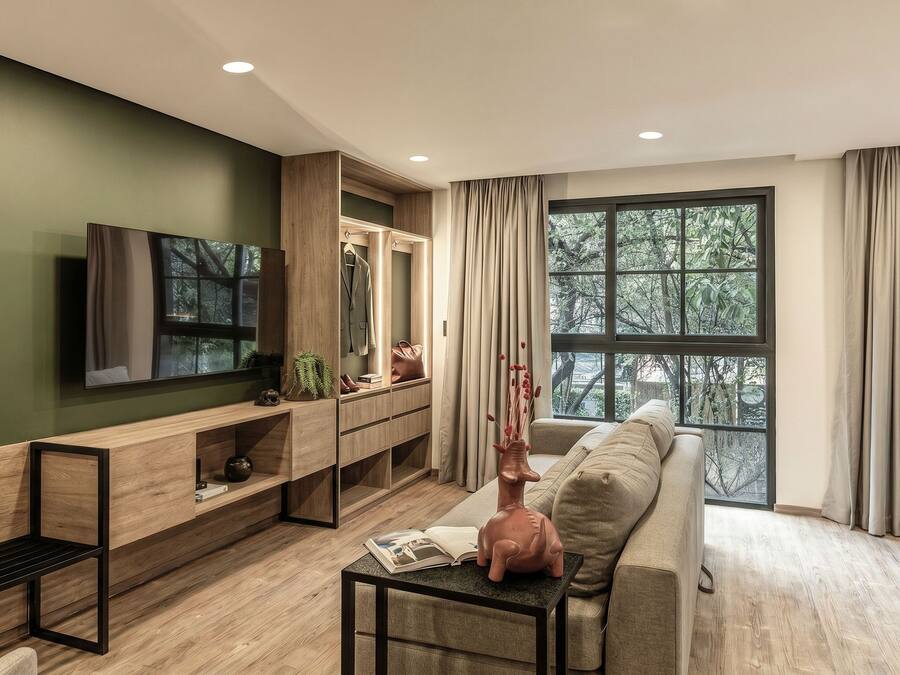 Una sala de estar moderna con televisor, sofá, consola de madera y un gran ventanal con cortinas.