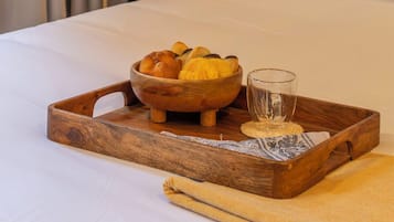 Une chambre d’hôtel avec un lit, un plateau en bois contenant du pain et un verre, et une table de chevet avec une lampe.