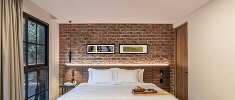 A modern hotel room with a brick wall, a large bed, a nightstand, and a window with curtains.