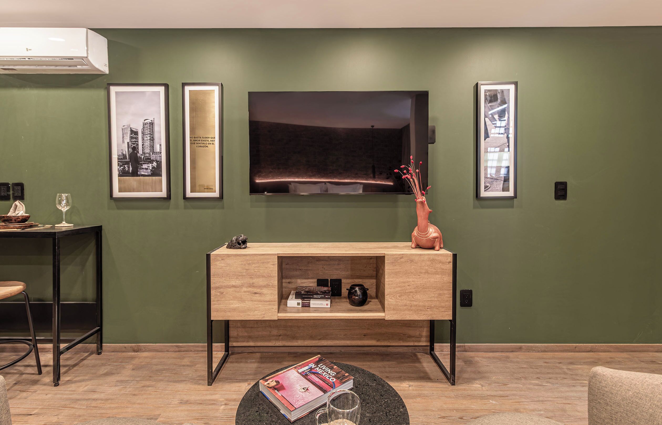 A living room with a TV, framed pictures, a wooden console, a round coffee table, and a magazine.