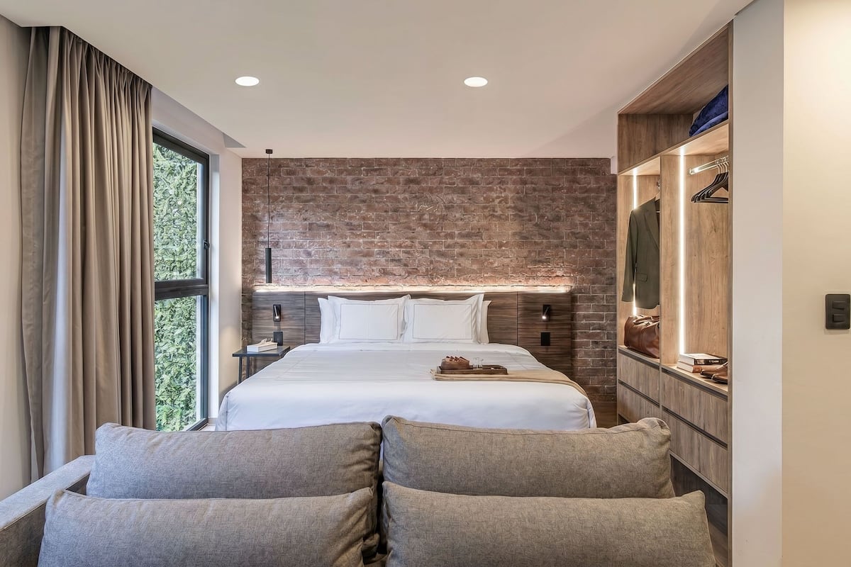 A modern bedroom with a large bed, a wooden wardrobe, and a view of greenery through the window.