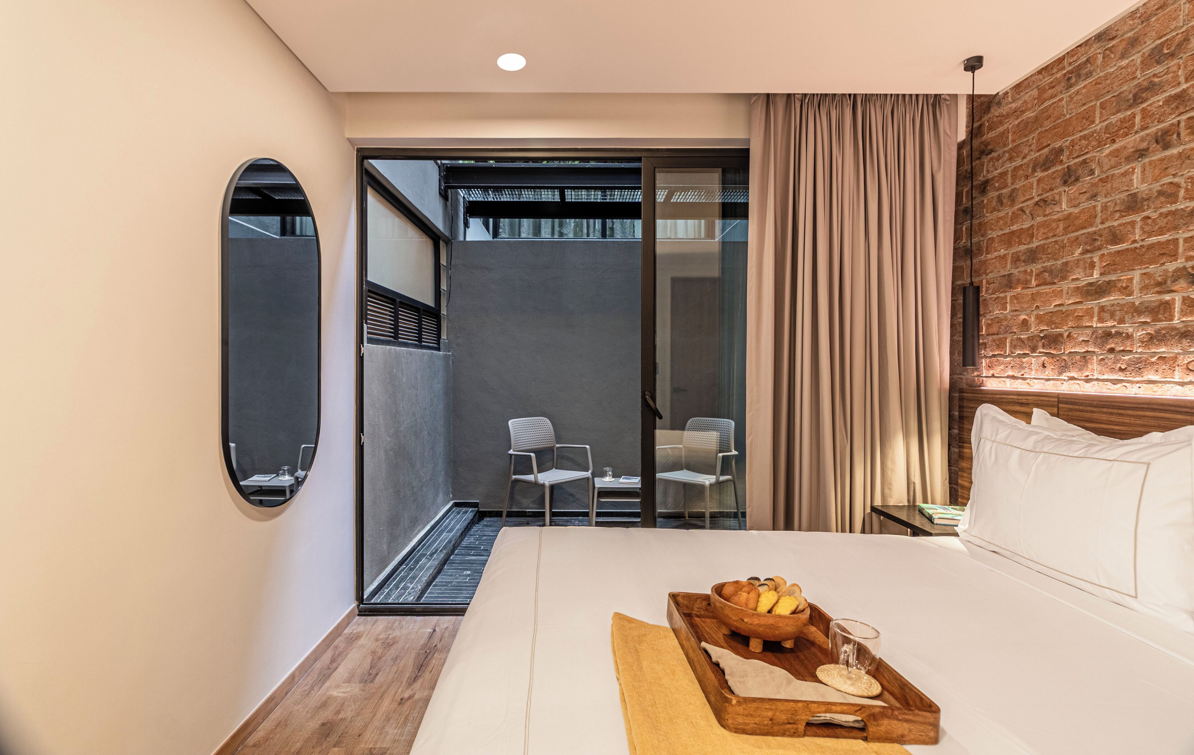 A hotel room with a bed, a breakfast tray, a mirror, and a view of the outside.