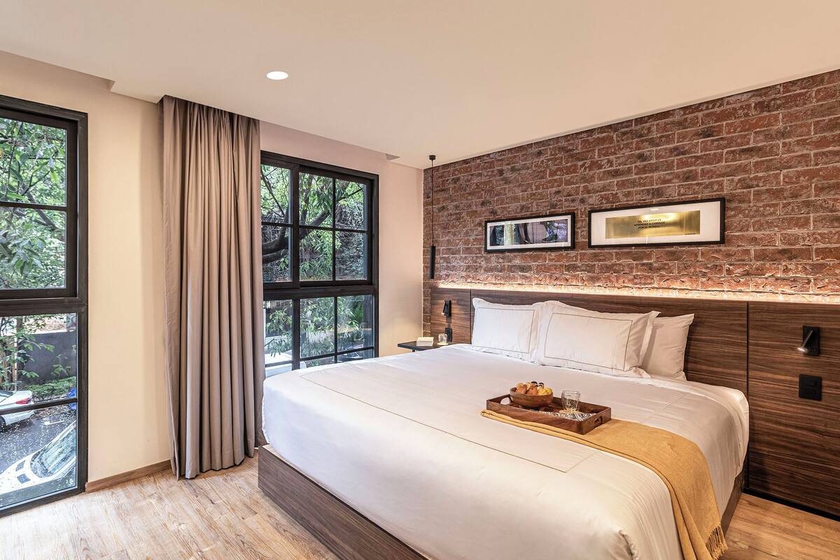 A modern bedroom with a large bed, a brick wall, and a view through a window.