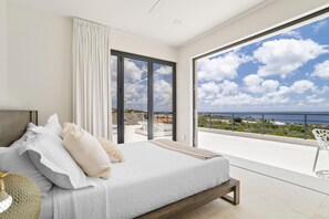 Une chambre avec un grand lit, une vue sur la mer et un balcon équipé d’une chaise.