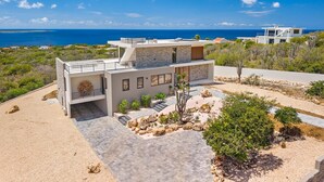 Una casa moderna de dos pisos con fachada de piedra, techo plano y vista al mar.